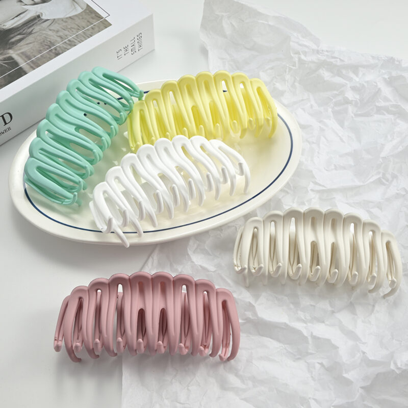 Five pastel candy-colored hollow large shark hair claw clips placed on white plate for women summer hairstyling