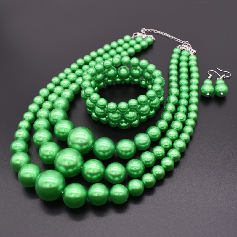 Multi-layer glossy green pearl matching jewelry set laid on dark background, consisting of necklace, bracelet and drop earrings for formal party and wedding outfit styling